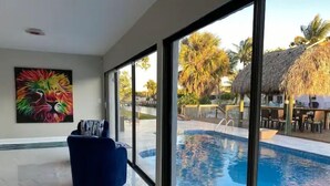 Ein modernes Zimmer mit großem Fenster und Blick auf einen Swimmingpool, einem farbenfrohen Löwenbild an der Wand und einem blauen Stuhl.