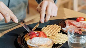 Una persona cortando un gofre con un cuchillo, rodeada de fresas y un pastel en un plato.
