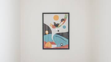Una habitación con un escritorio y una silla de madera, una obra de arte abstracta enmarcada en la pared, y una pared blanca lisa.