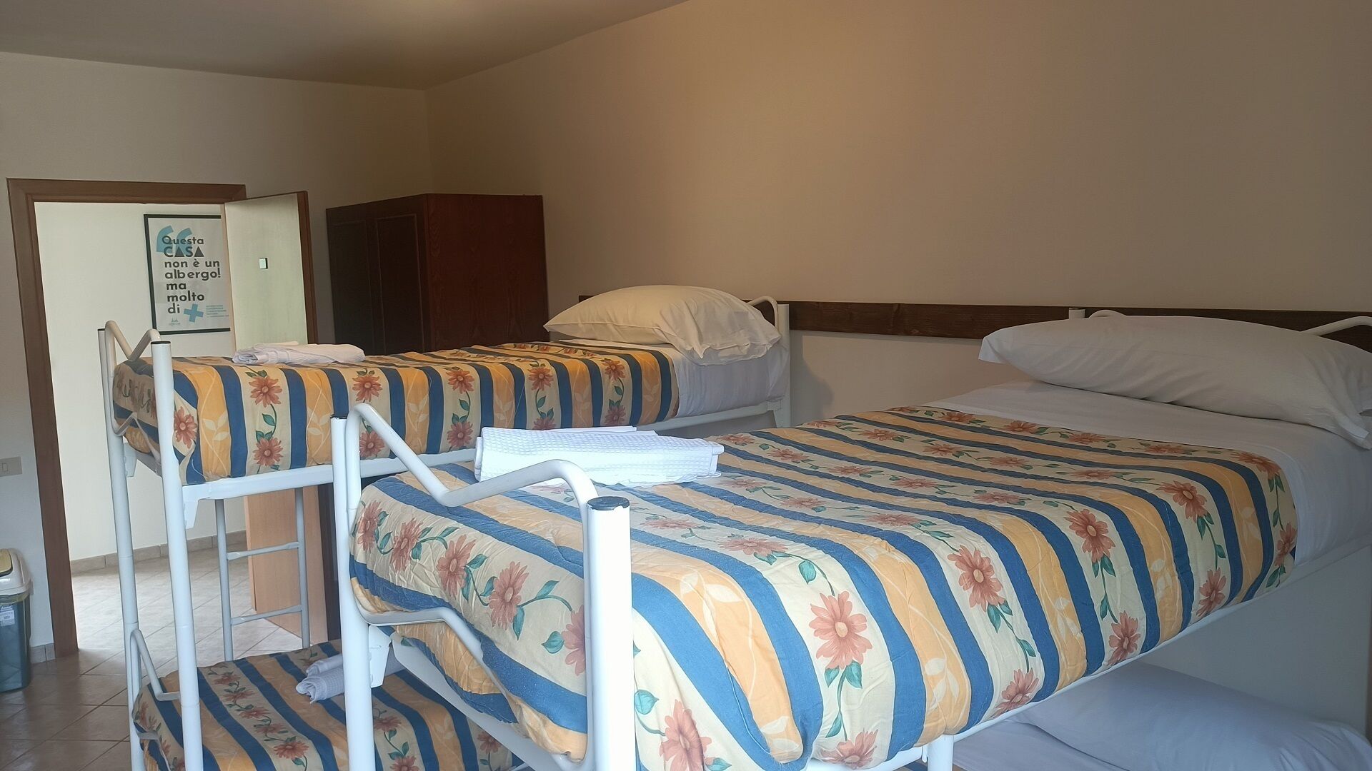 Een slaapzaal met twee bedden, een houten kledingkast en een kleine prullenbak.