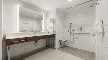 A modern bathroom with a large mirror, a wooden vanity, a shower area, and a towel rack.
