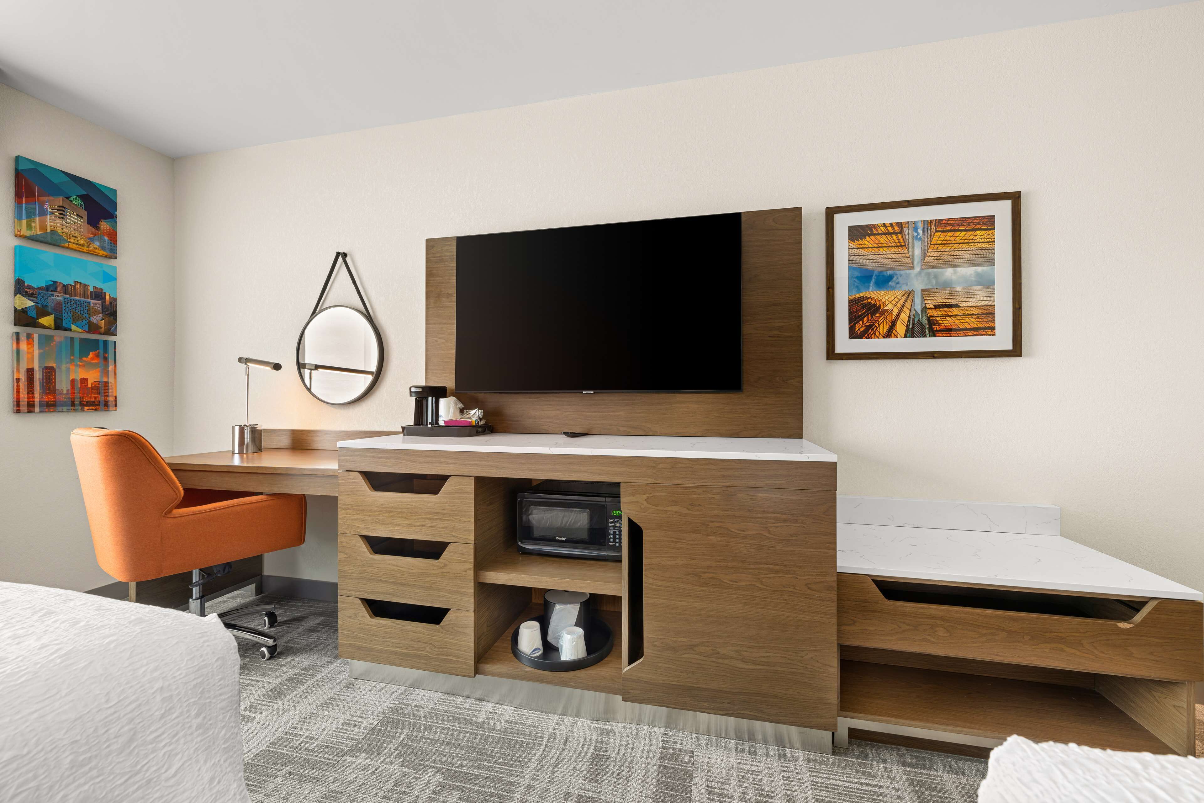 Ett modernt hotellrum med ett skrivbord i trä, en platt-TV, en mikrovågsugn och en säng.