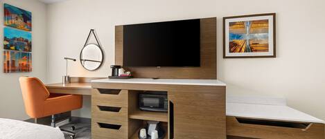 A modern hotel room with a wooden desk, a flat-screen TV, a microwave, and a bed.