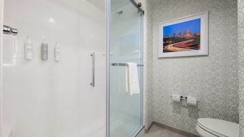 Casa de banho moderna com cabine de duche em vidro, sanita e quadro com uma vista urbana emoldurada na parede.