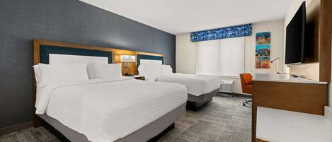 A hotel room with two beds, a desk, a chair, a television, and artwork on the wall.