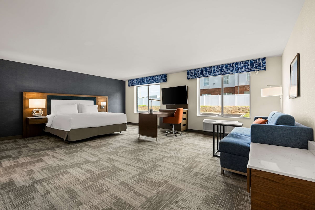 A hotel room with a bed, desk, chair, and a sofa.
