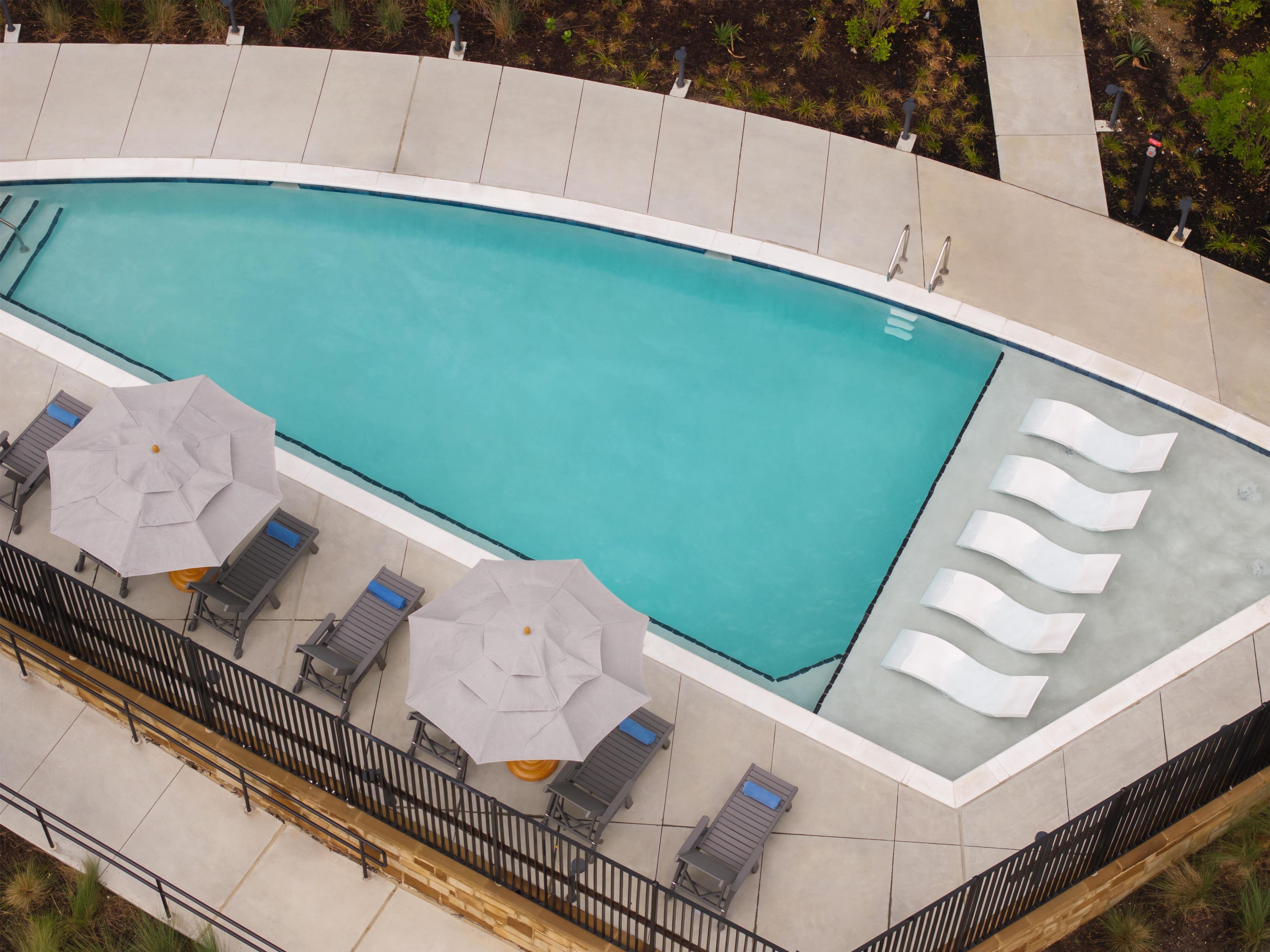 A swimming pool with lounge chairs and umbrellas, surrounded by a tiled deck.