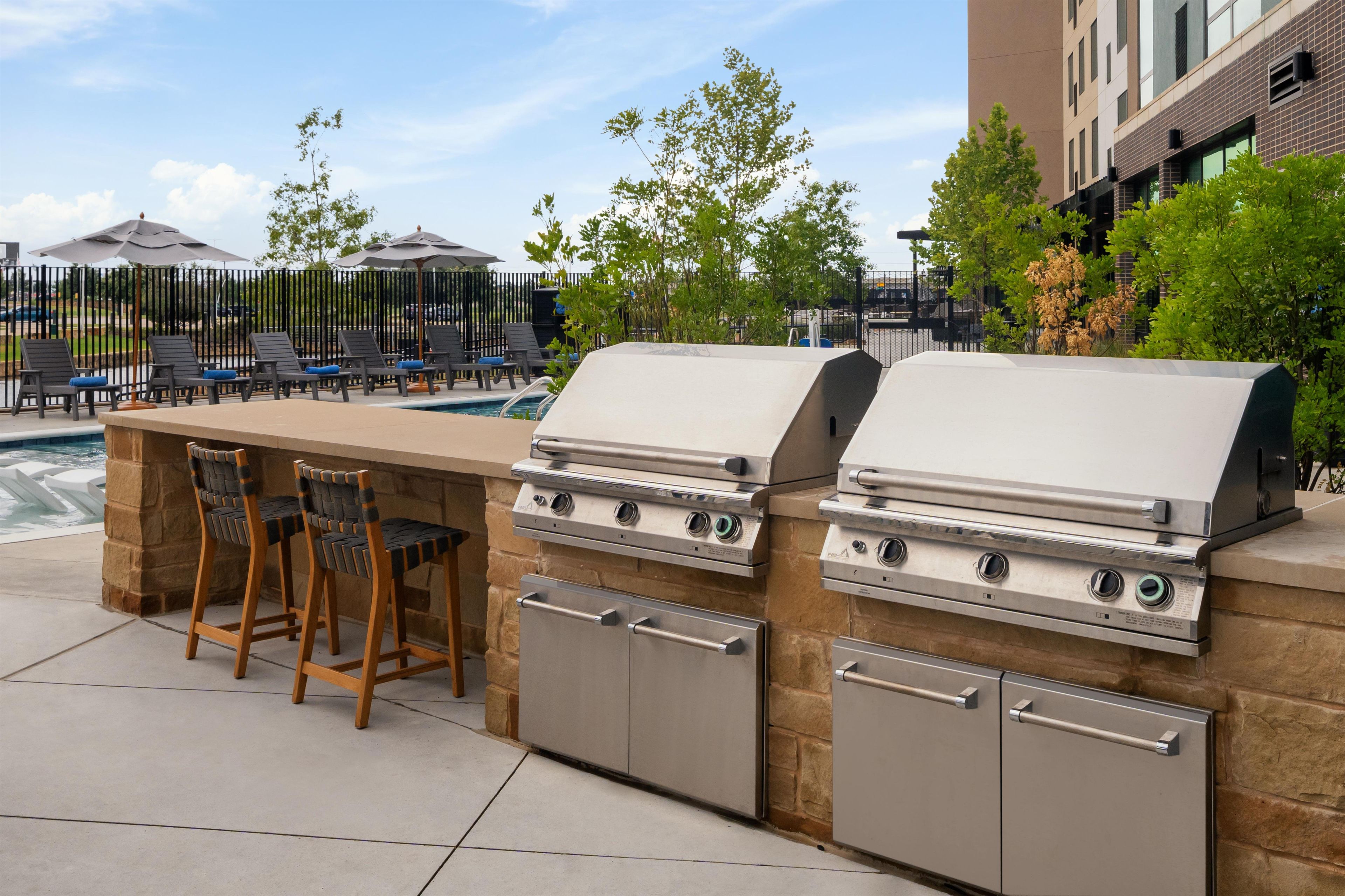 An outdoor kitchen with a grill, bar stools, and a poolside area.
