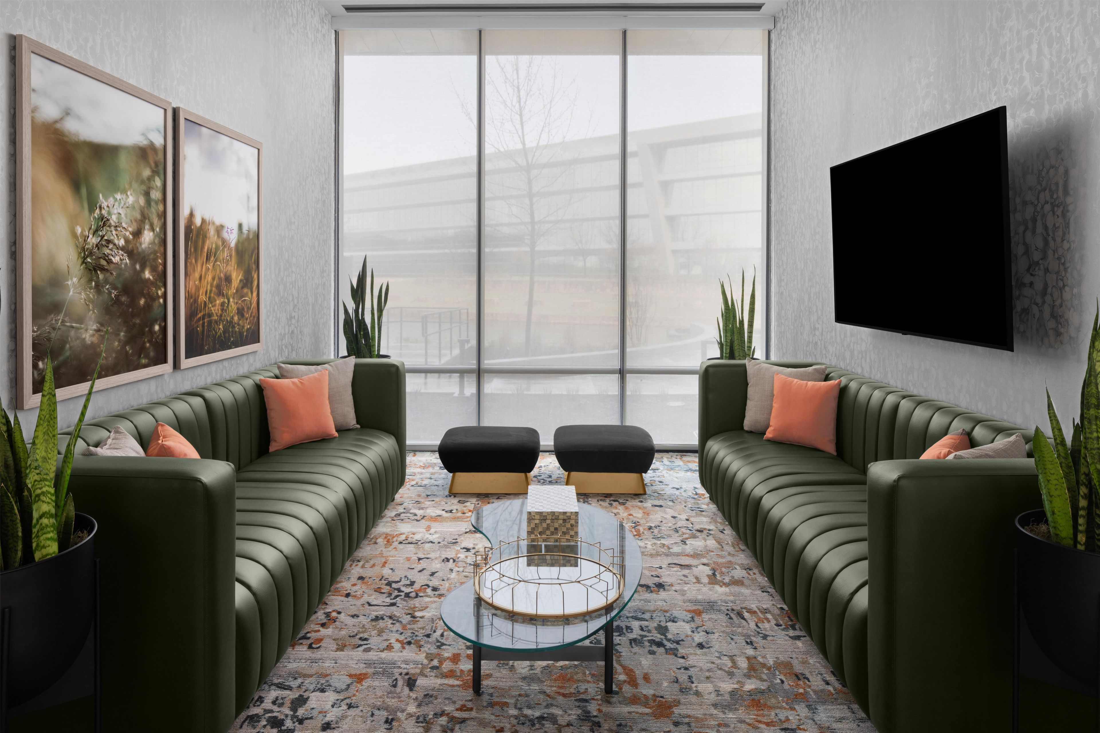A modern living room with a green sofa set, a glass coffee table, and a large window.