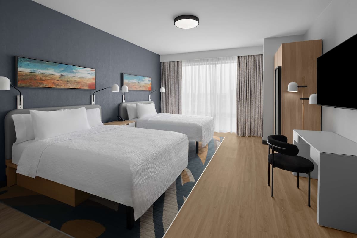 A modern hotel room with two beds, a desk, a chair, a flat-screen TV, and a painting on the wall.