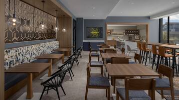 Un restaurante moderno con mesas y sillas de madera, un muro con diseño y vistas a la ciudad.