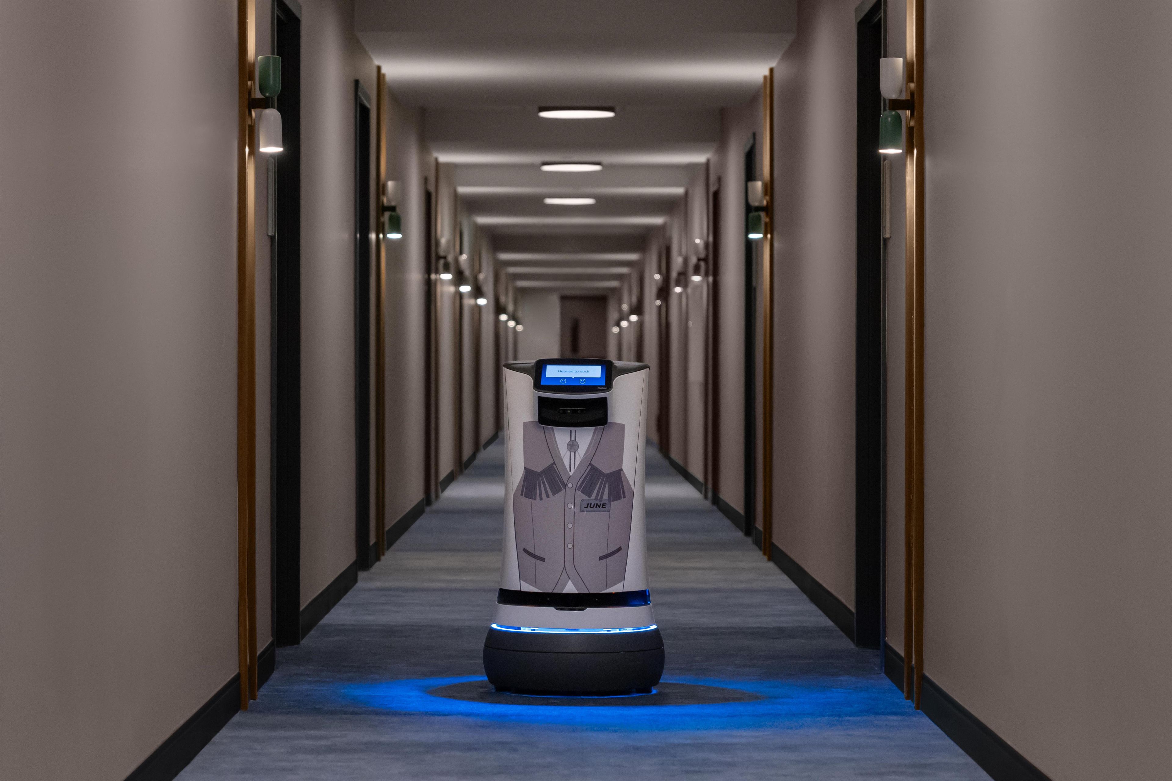 Un robot dans un couloir d’hôtel, avec un sol illuminé d’une lumière bleue.