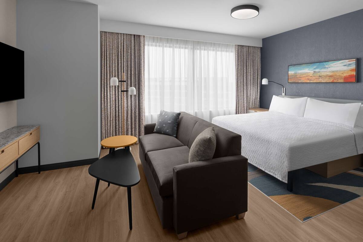 A modern hotel room with a bed, a sofa, a small table, and a TV.