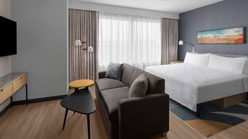 A modern hotel room with a bed, a sofa, a small table, and a TV.