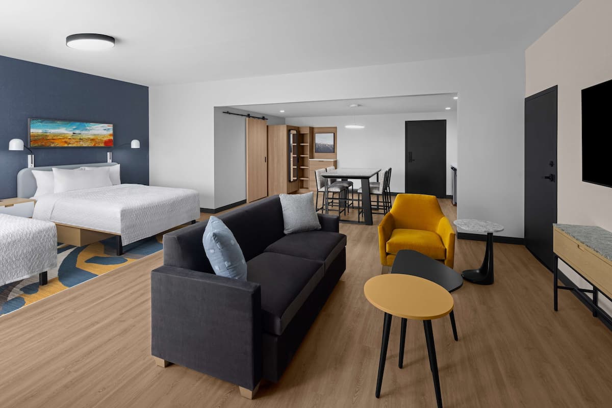 A modern hotel room with a bed, sofa, dining table, and chairs.