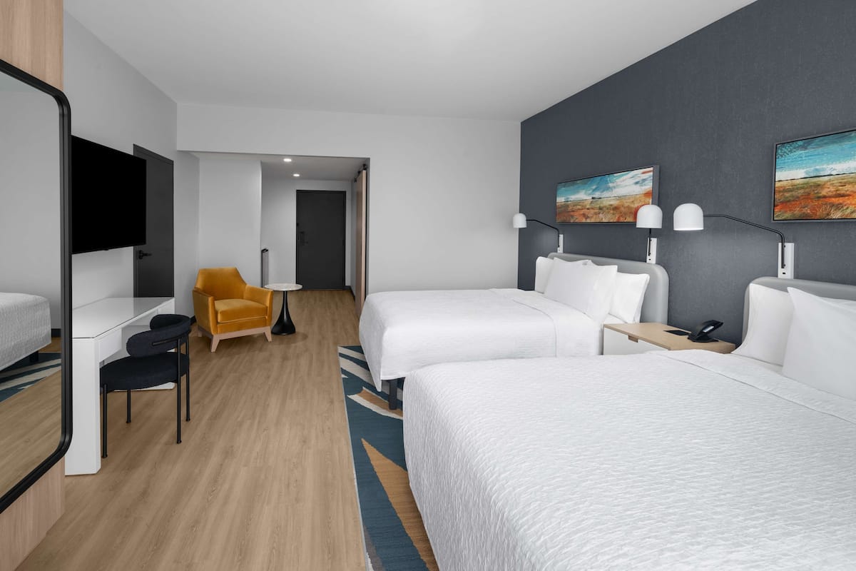 A modern hotel room with two beds, a desk, a chair, and a TV.