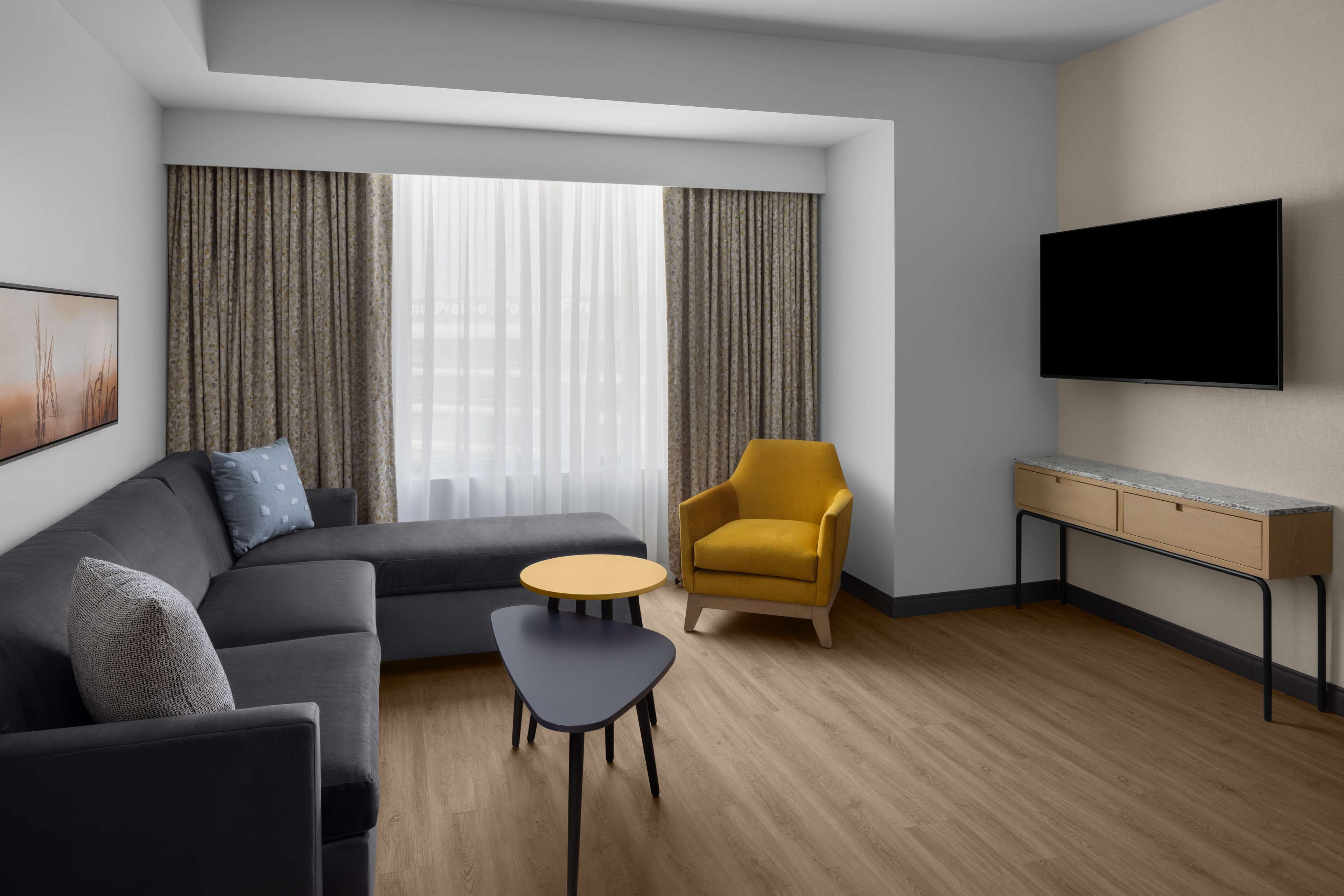 Un salon moderne avec un canapé, une petite table, un fauteuil jaune et un téléviseur fixé au mur.