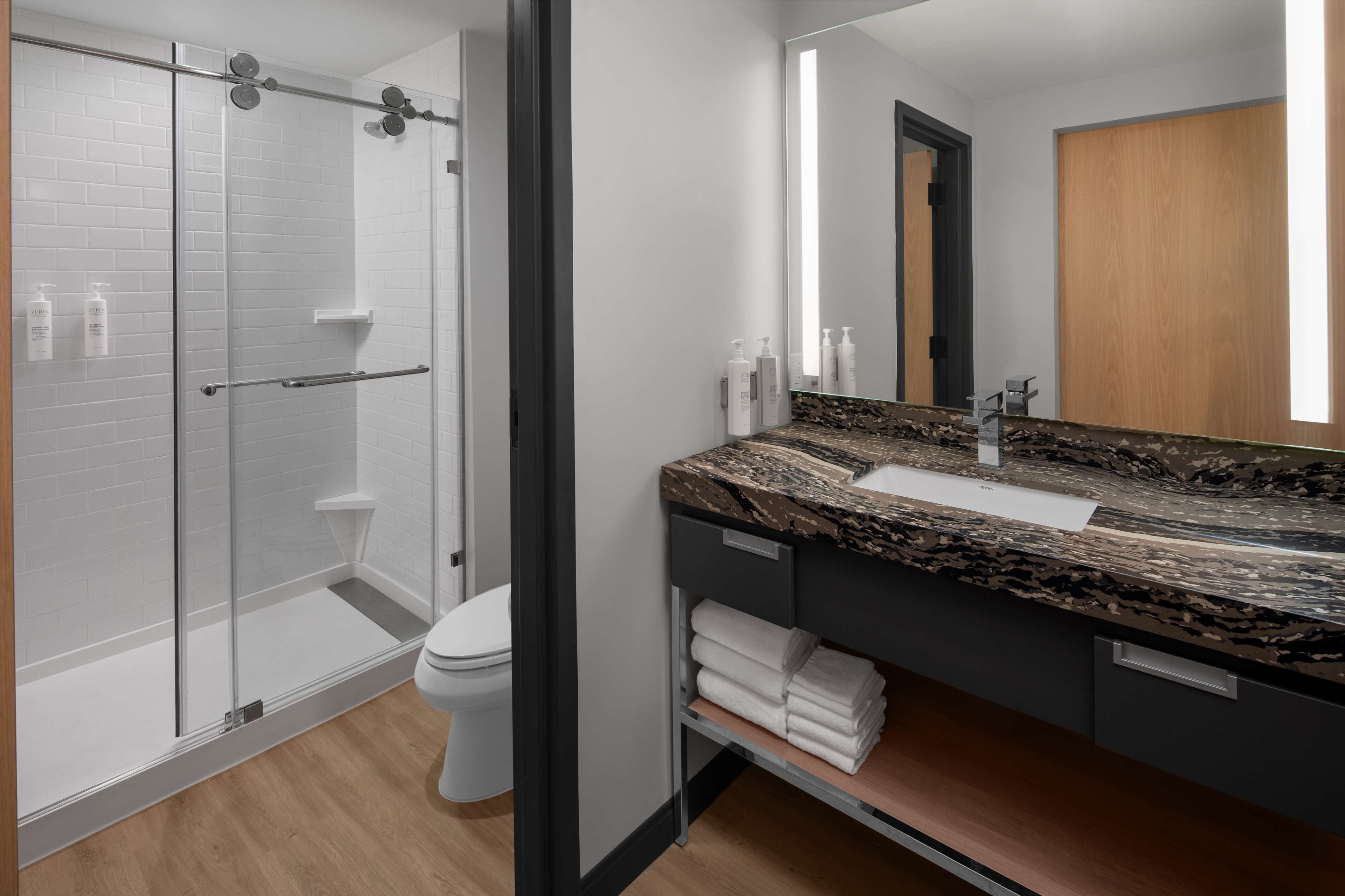 A modern bathroom with a glass shower enclosure, a white toilet, a marble sink, and a wooden vanity.