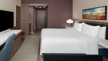 A hotel room with a bed, a desk with a chair, a TV, and a painting on the wall.