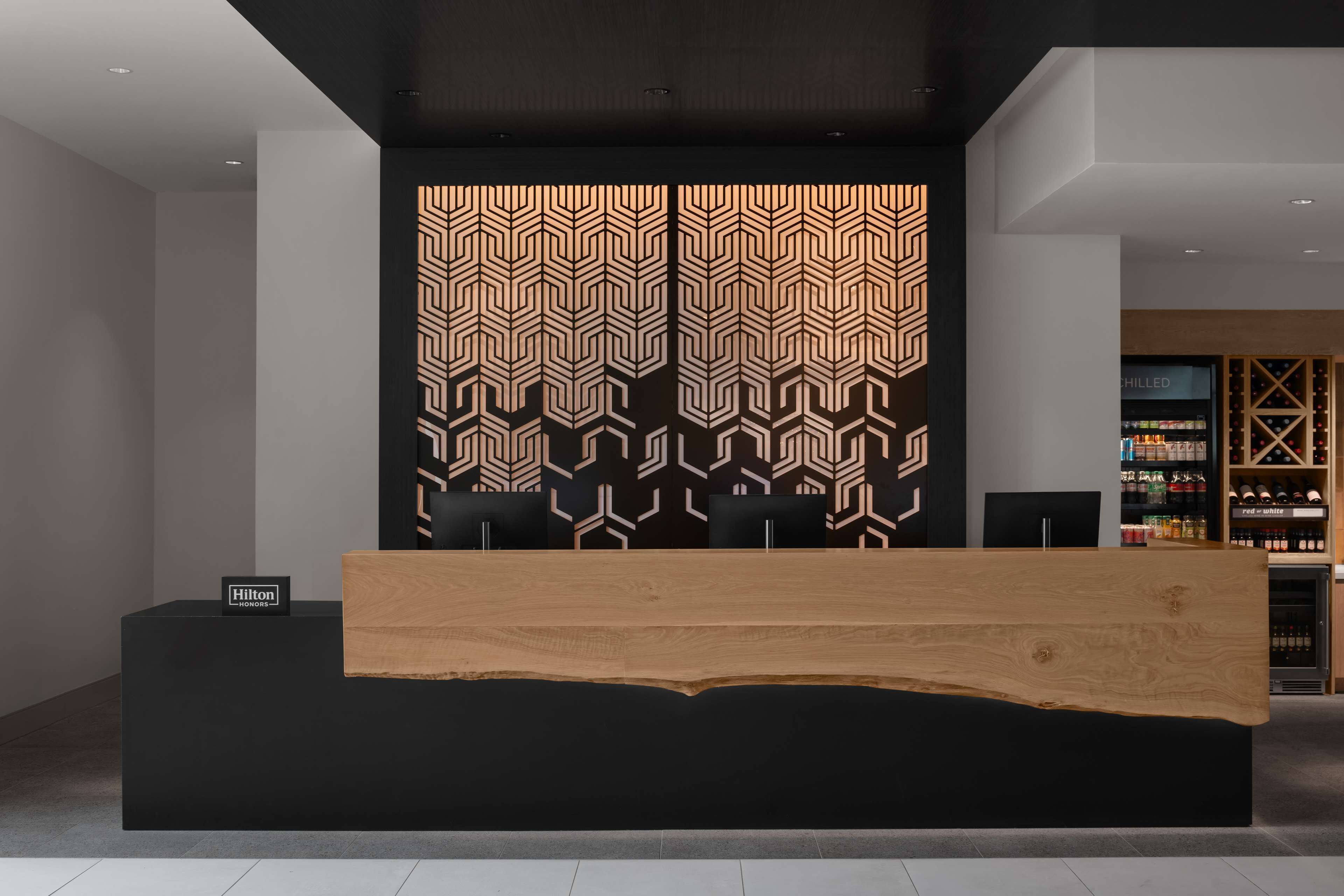 A reception desk with a modern design, a black and white patterned wall, and a minibar area in the background.
