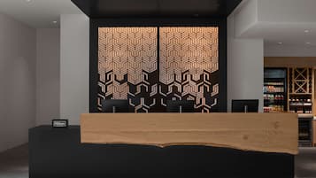 A reception desk with a modern design, a black and white patterned wall, and a minibar area in the background.