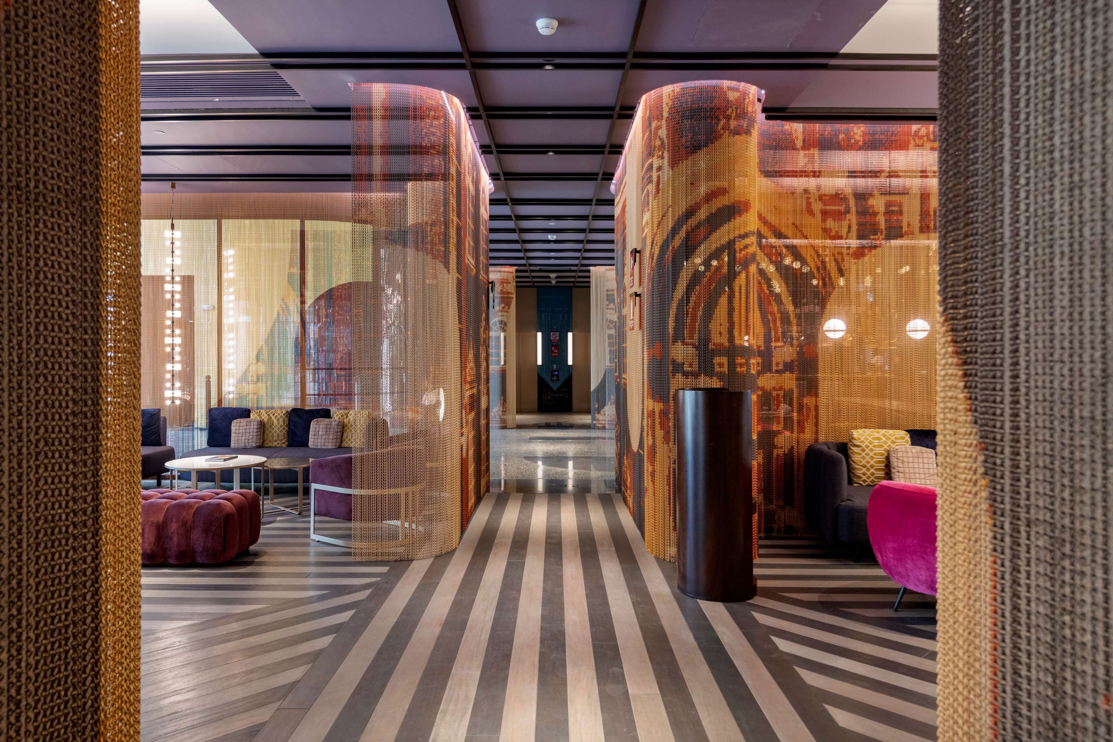 En moderne hotellobby med striberet gulv, siddeområder og dekorative søjler.