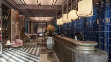 A modern hotel lobby with a reception desk, seating area, and a large window.