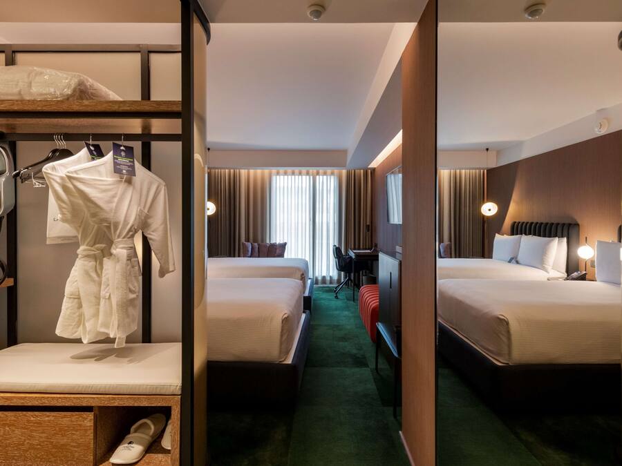 A hotel room with two beds, a desk, a chair, a robe, slippers, and a hairdryer.