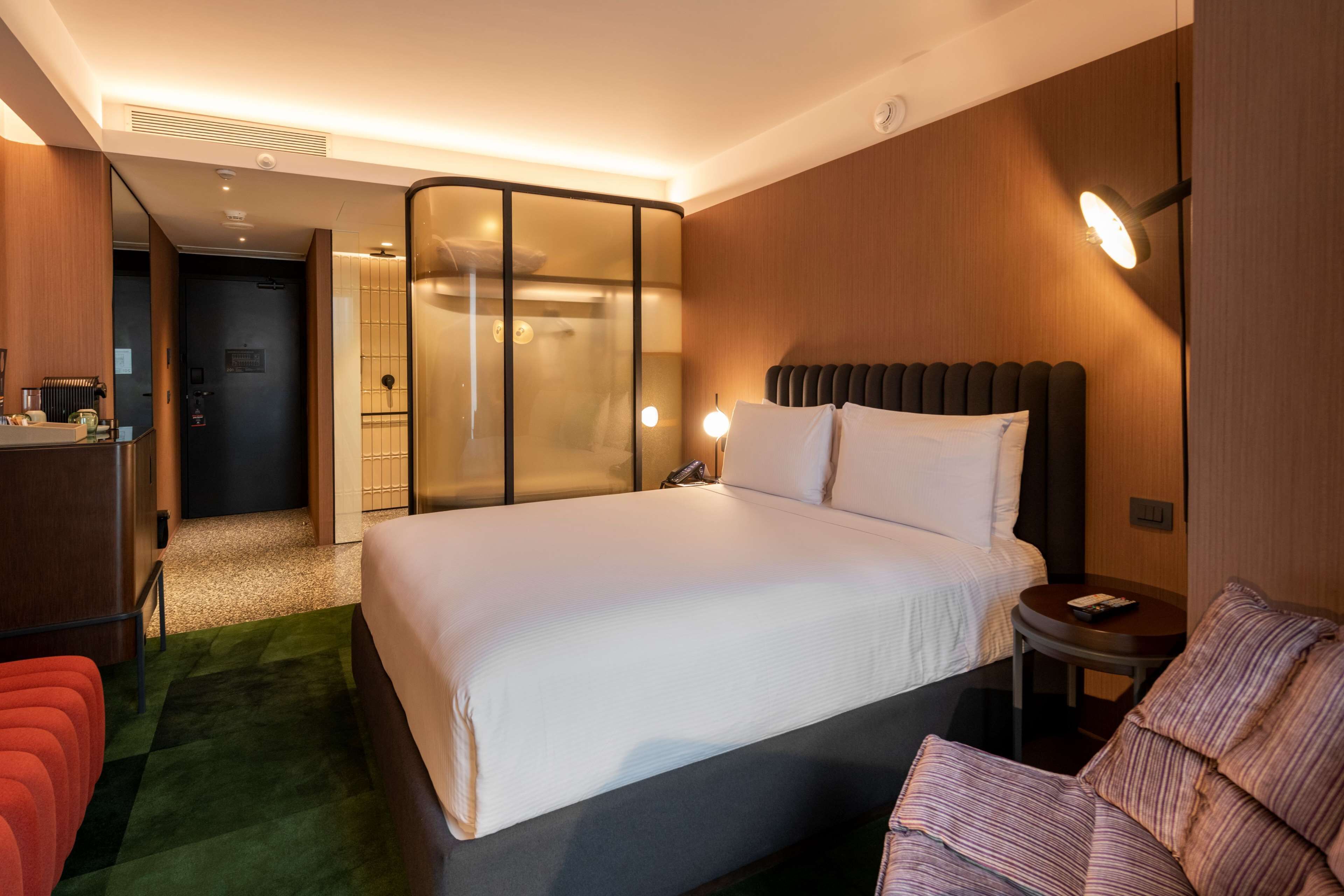 Una camera d'albergo con un letto grande, un tavolino, una sedia e una zona salotto separata con un divano.