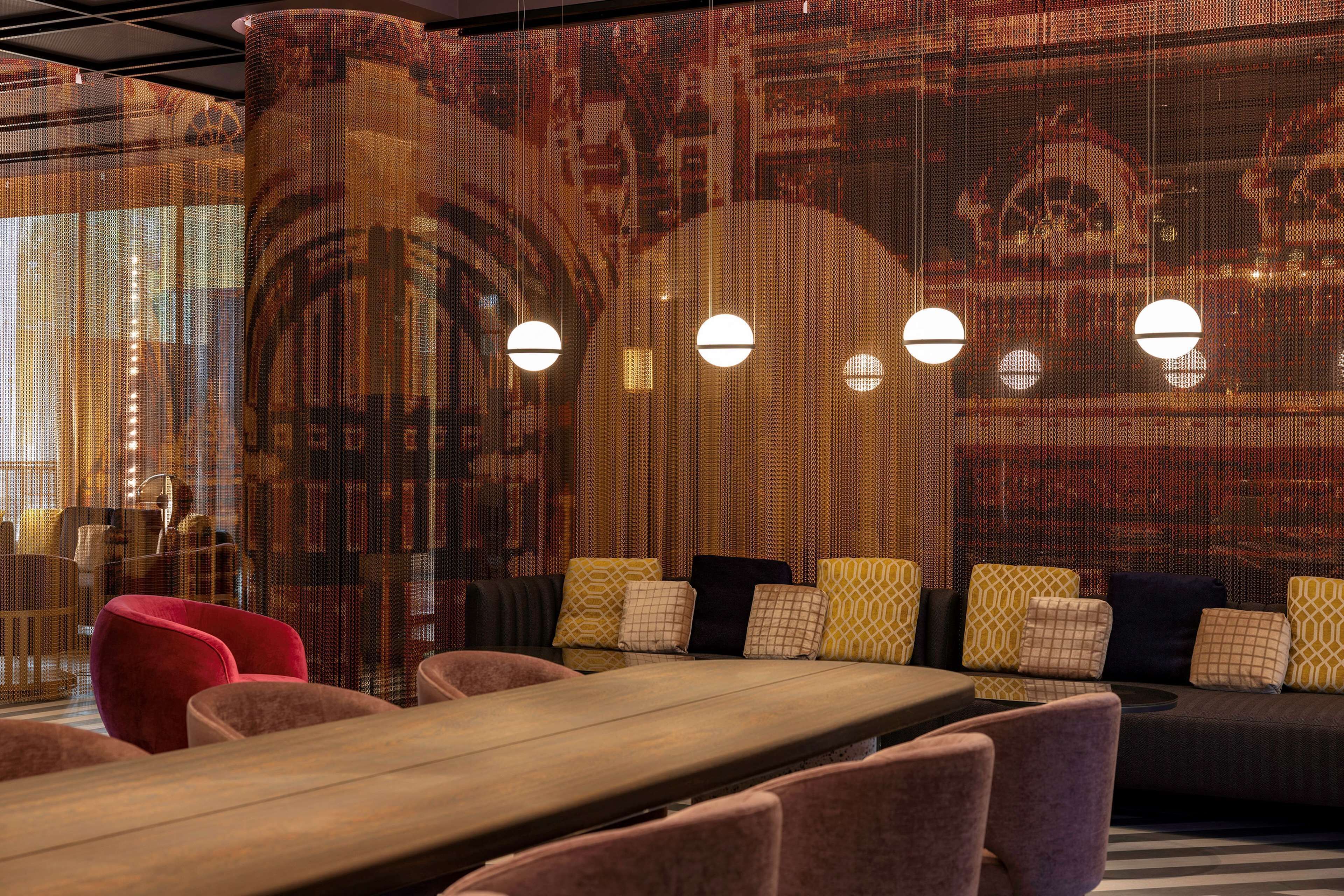 A modern lounge area with a long wooden table, several cushioned seating options, and pendant lighting.