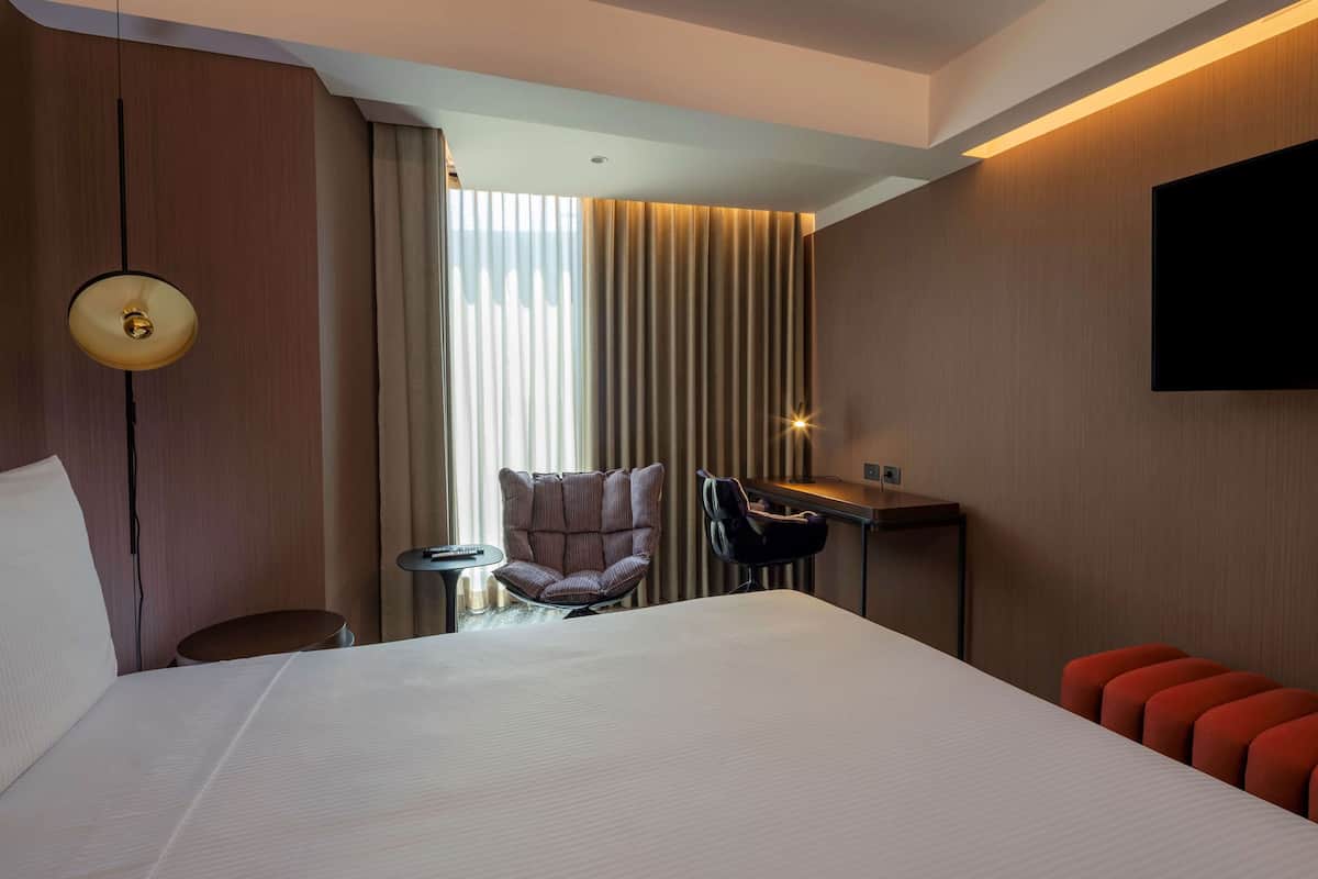 A hotel room with a large bed, a desk, a chair, and a TV mounted on the wall.