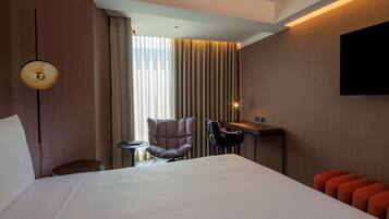 A hotel room with a large bed, a desk, a chair, and a TV mounted on the wall.