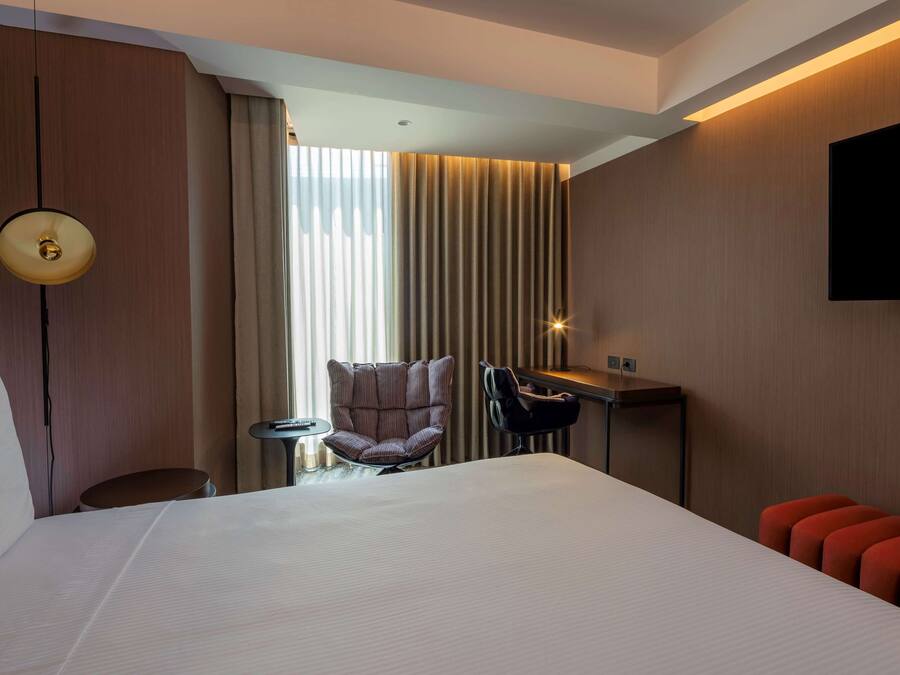 A hotel room with a large bed, a desk, a chair, and a TV mounted on the wall.