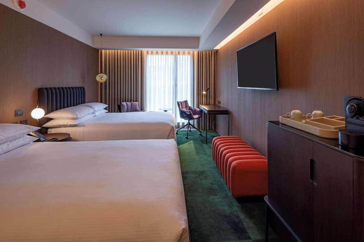 A hotel room with two beds, a desk, a chair, a TV, and a minibar.
