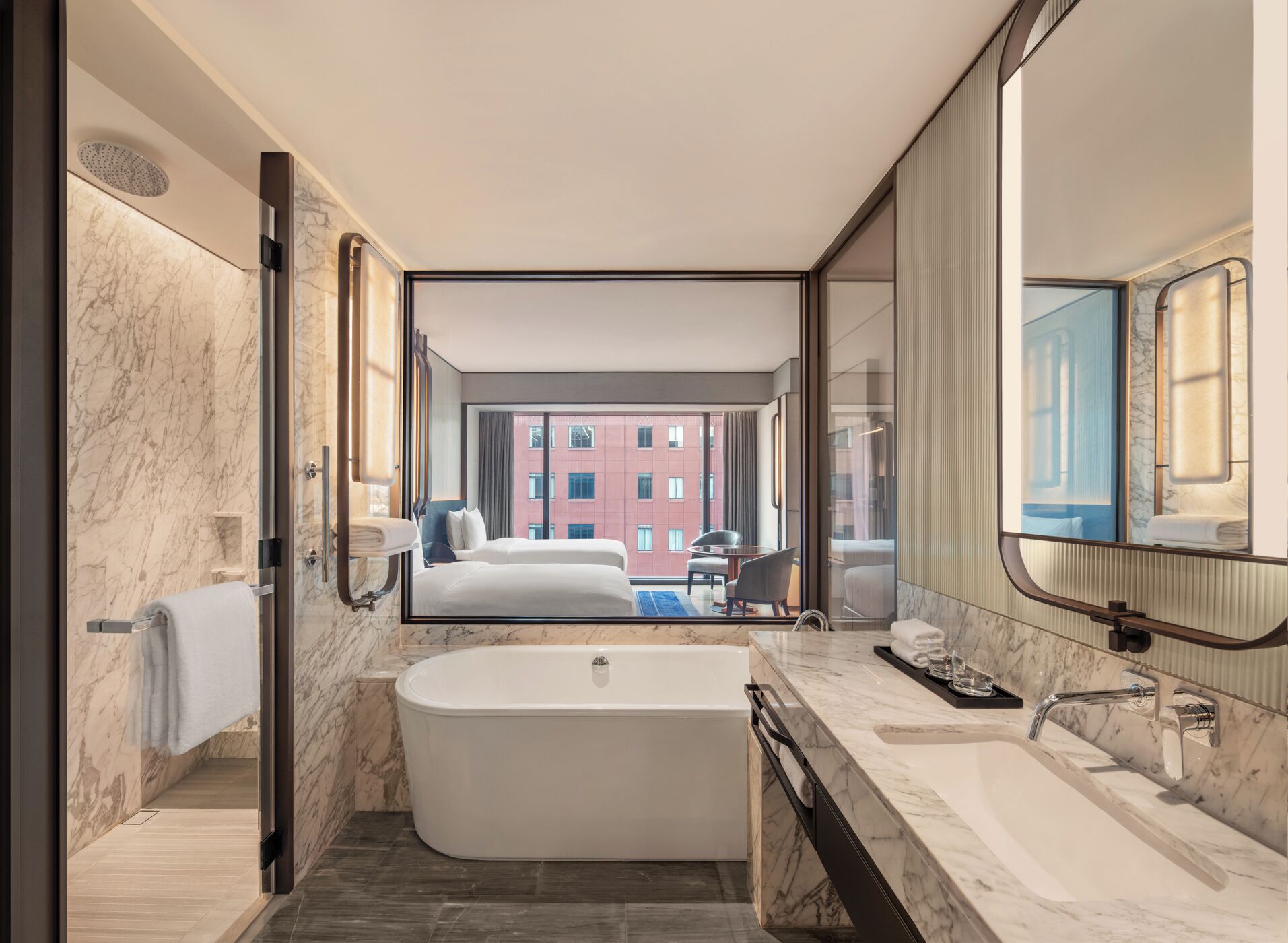 A modern hotel bathroom with a large bathtub, a separate shower area, and a large mirror reflecting the room.