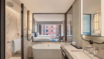 A modern hotel bathroom with a large bathtub, a separate shower area, and a large mirror reflecting the room.