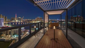 A modern rooftop terrace with a city view, featuring a wooden floor, two tables with candles, and a glass railing. - Hilton Saigon (Ho Chi Minh City)
