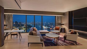 A modern hotel room with a large panoramic window, a dining area, and a seating area with a view of the cityscape. - Hilton Saigon (Ho Chi Minh City)