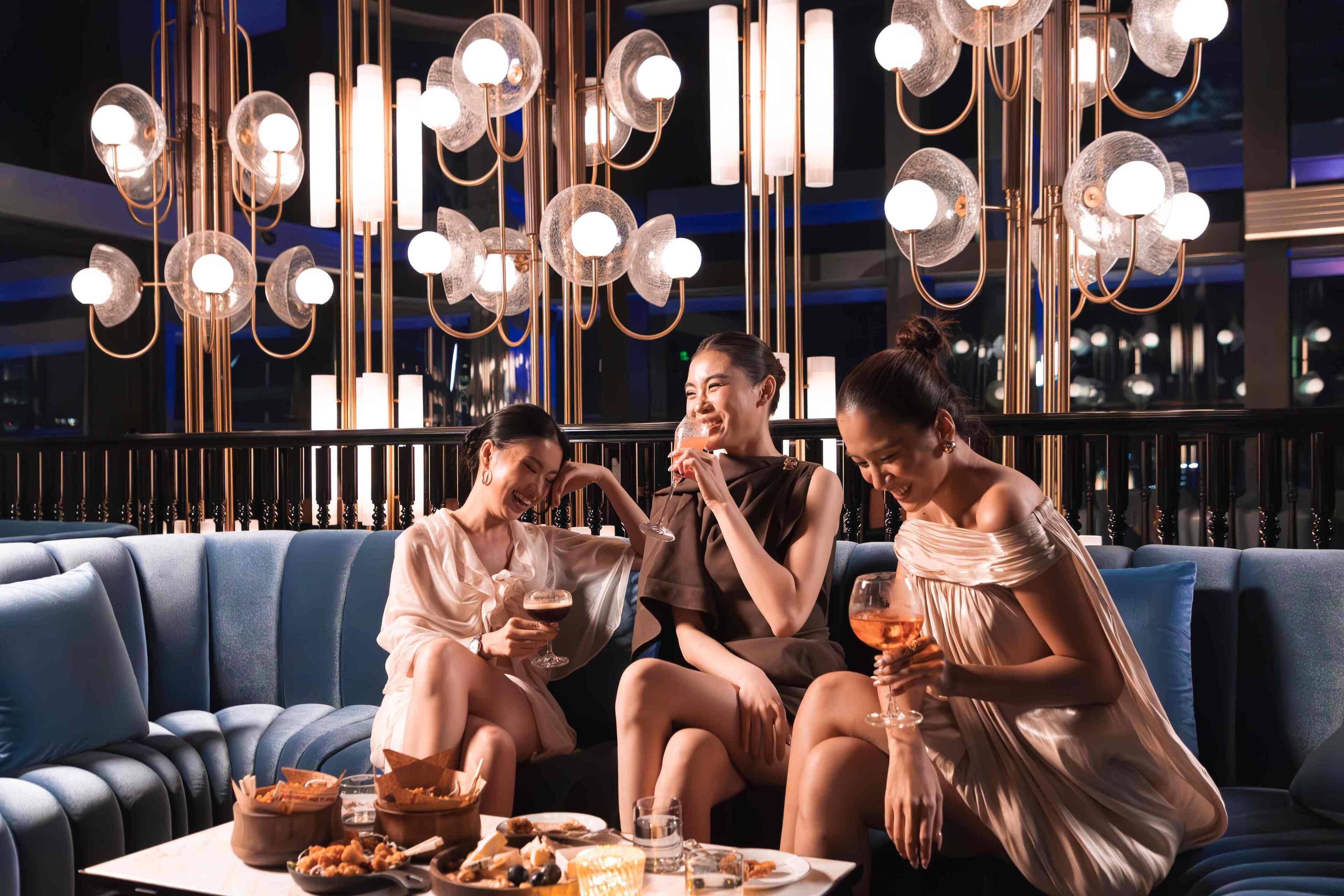 A group of people sitting on a blue sofa in a well-lit room with modern chandeliers.