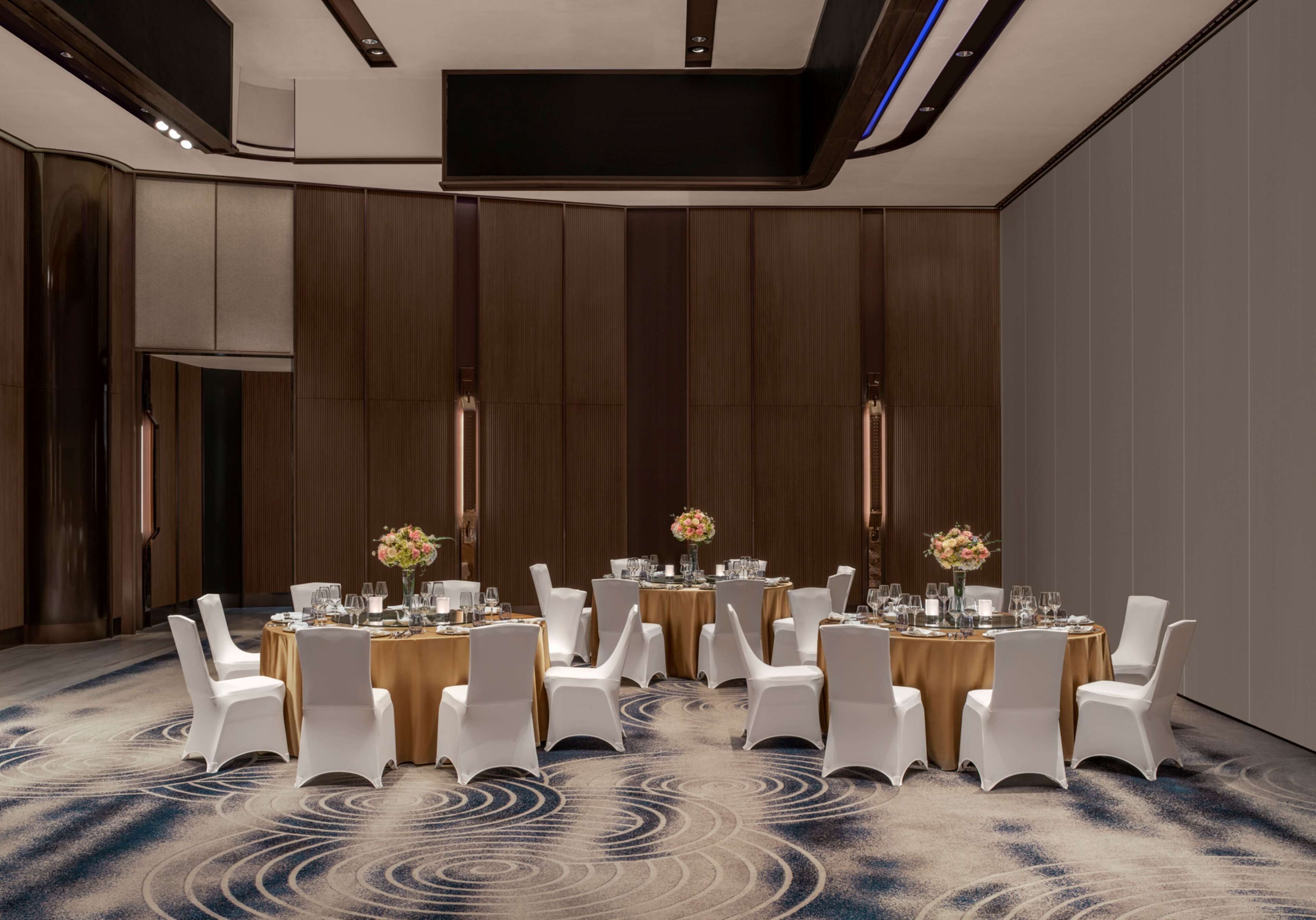 A conference room with round tables, white chairs, and floral centerpieces.