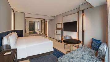 Ein modernes Hotelzimmer mit einem großen Bett, einem Schreibtisch, einem Sessel, einer Couch, einem Fernseher und einem Spiegel.