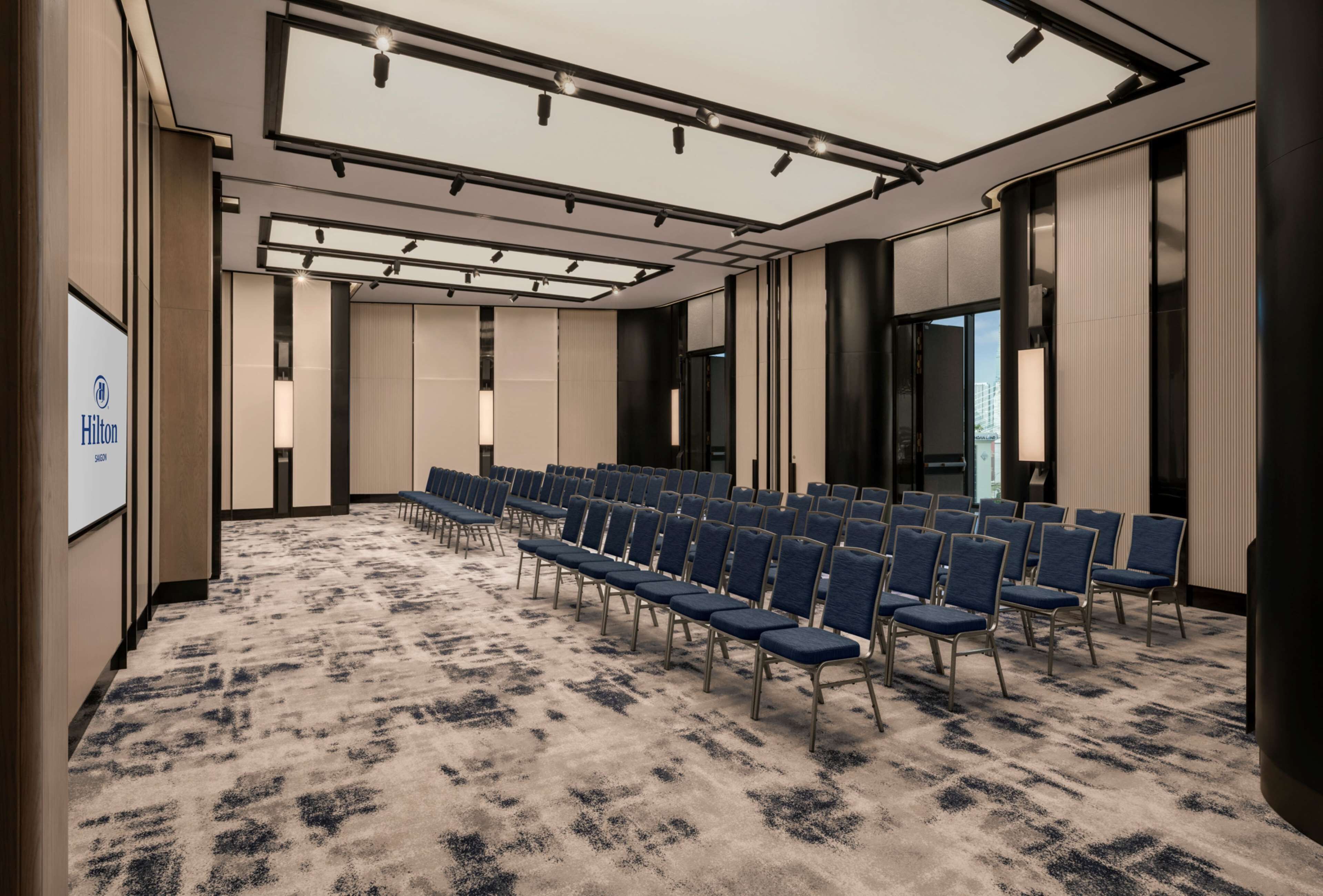 A conference room with rows of chairs, a carpeted floor, and a large screen on the left.