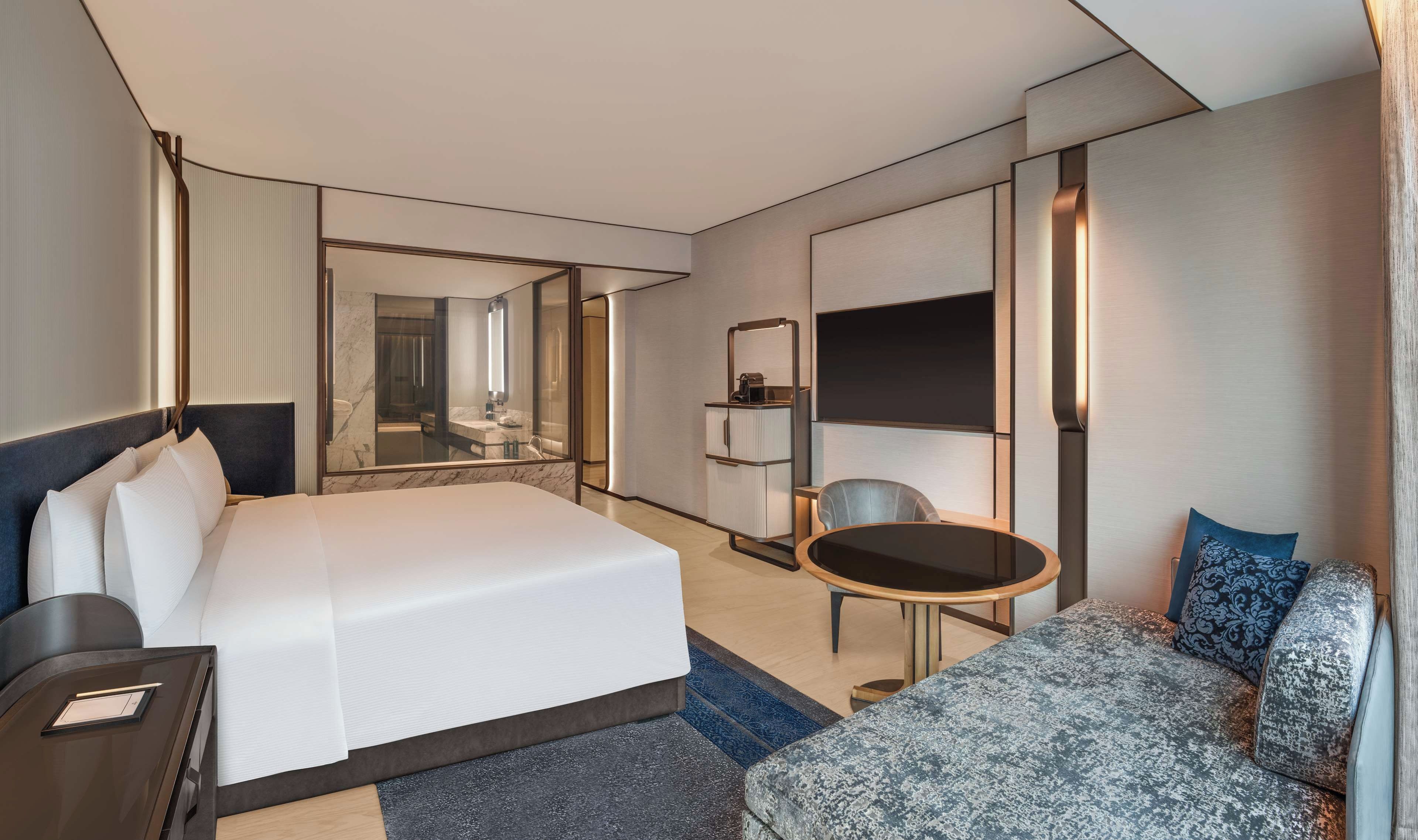 A modern hotel room with a large bed, a seating area with a table, a TV, and a mirror.
