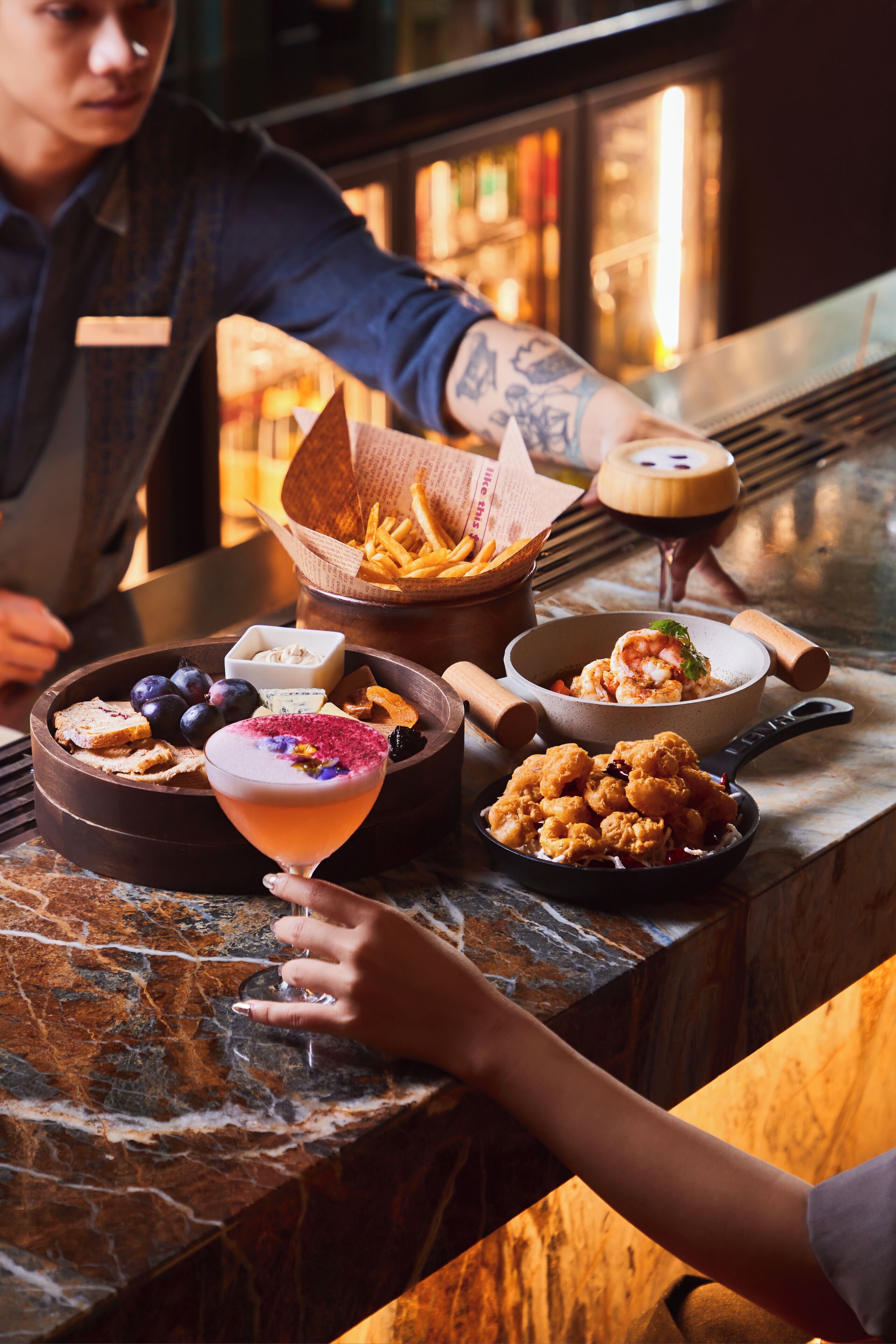 Un bar con mostrador de mármol, un cóctel y diferentes opciones de comida, incluyendo un bol de camarones y una cesta de papas fritas.