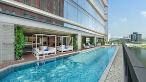 A modern indoor pool with lounge areas, a view of the city skyline, and a glass facade building in the background. - Hilton Saigon (Ho Chi Minh City)