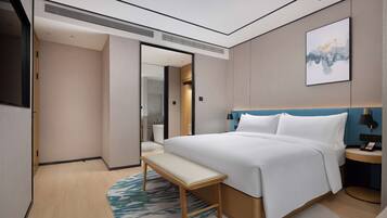 Una habitación de hotel moderna con una cama grande, un banco, una mesita de noche y un buró.