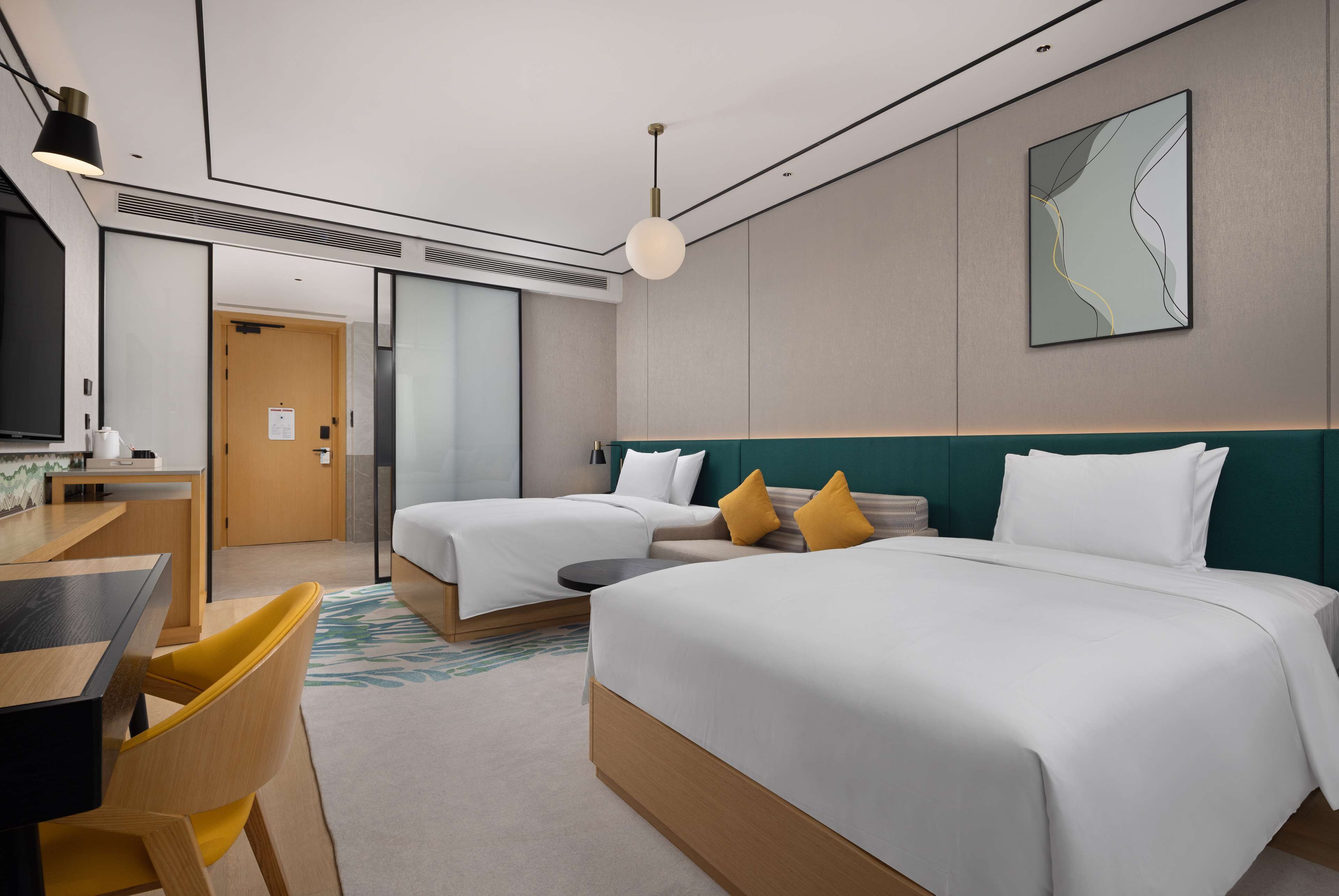 A hotel room with two beds, a desk, and a chair. There is a television on the left and a painting on the wall.