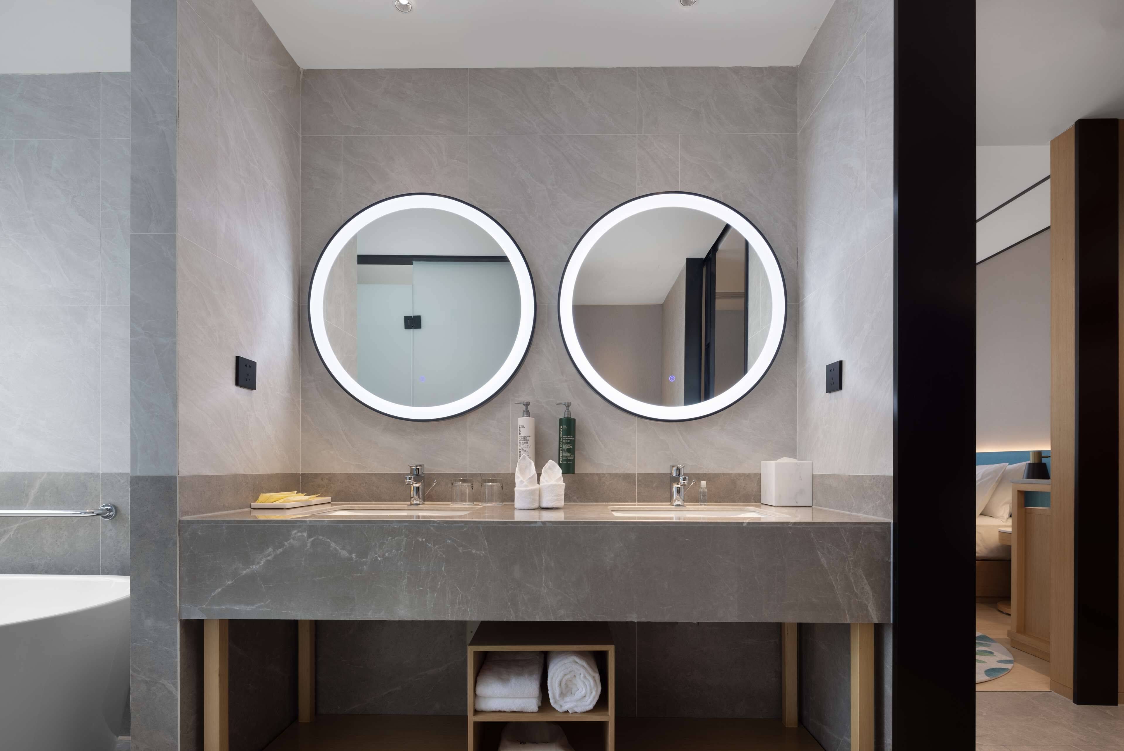 Une salle de bain moderne avec deux miroirs ronds, un comptoir en marbre et une étagère à serviettes.