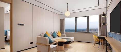 A modern living room with a sofa, chairs, a round table, and a large window with a city view.