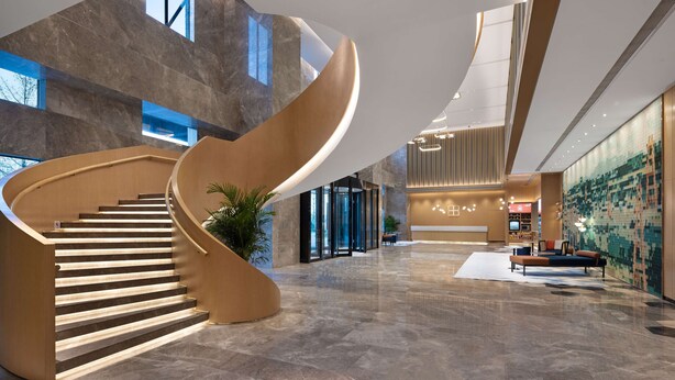 A modern lobby with a curved staircase, a reception area, and a seating area. - Hilton Garden Inn Zigong High-Tech Zone (Zigong)